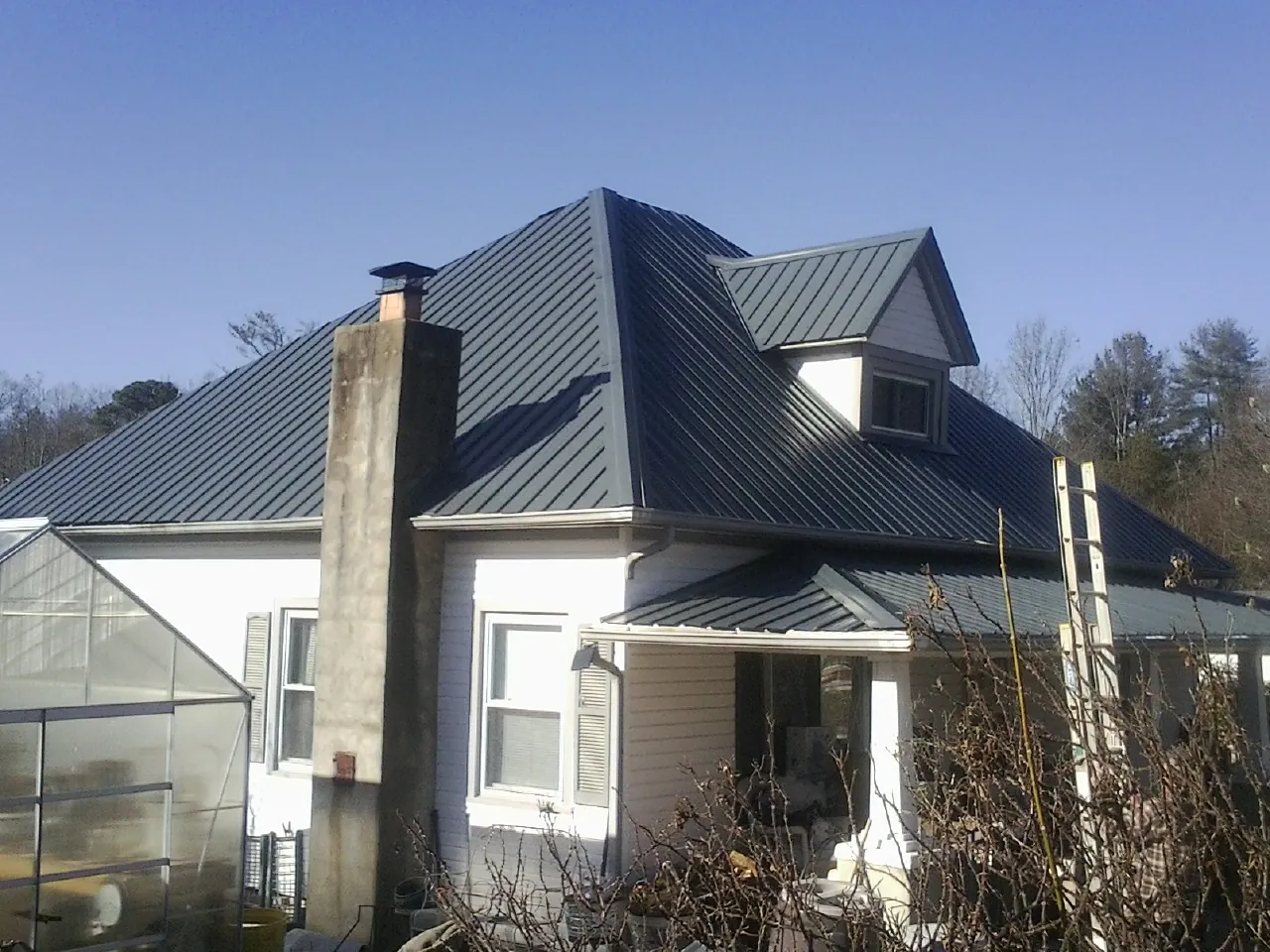 Dark blue standing seam metal roof on a white farmhouse with dormer — Slate & Tile Roof Repair by Roofing Brothers in Sodus