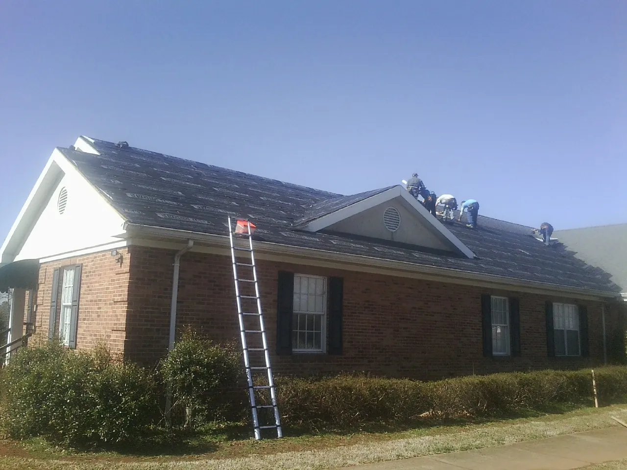 Crew tearing shingles off a brick ranch roof with a ladder set — Metal Roof Repair work by our crew in Sodus
