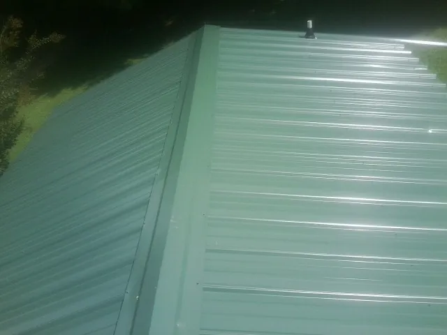 New green metal panels meeting at the ridge of a roof — Flat Roof Repair work by our crew in Sodus