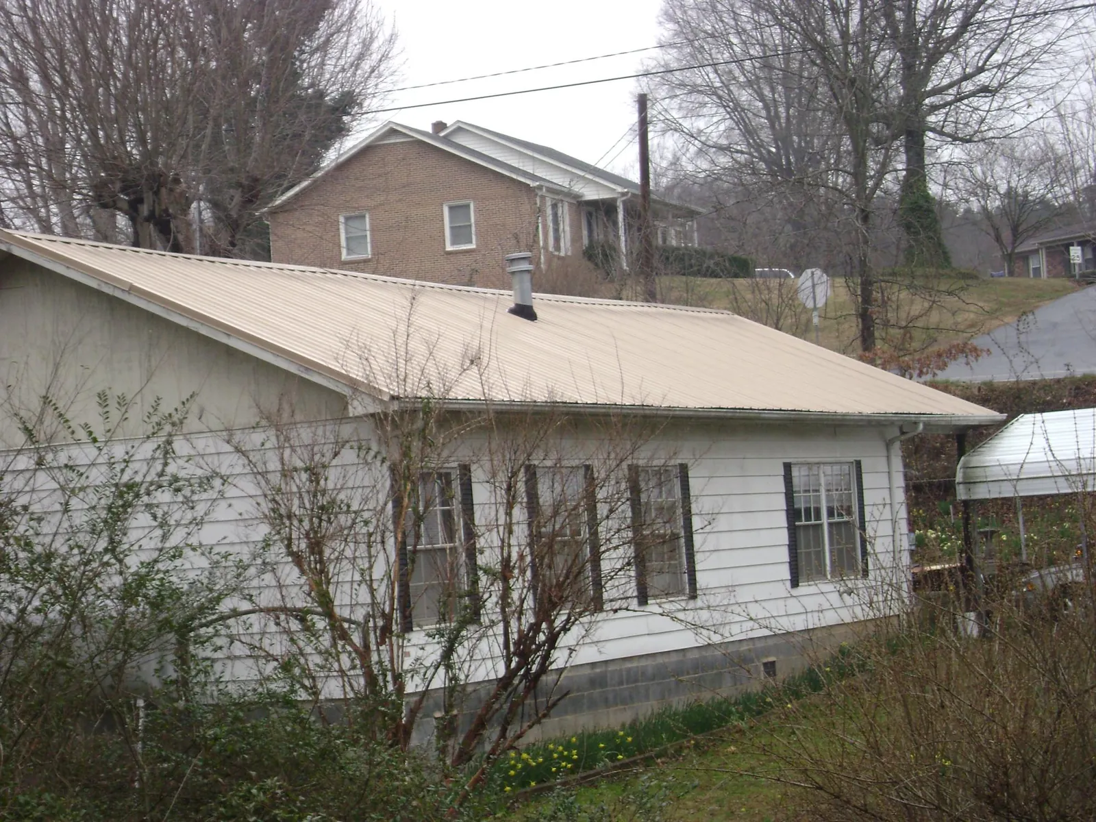 Tan metal roof on a white sided house set into a hillside — Commercial Roofing by Roofing Brothers in Sodus
